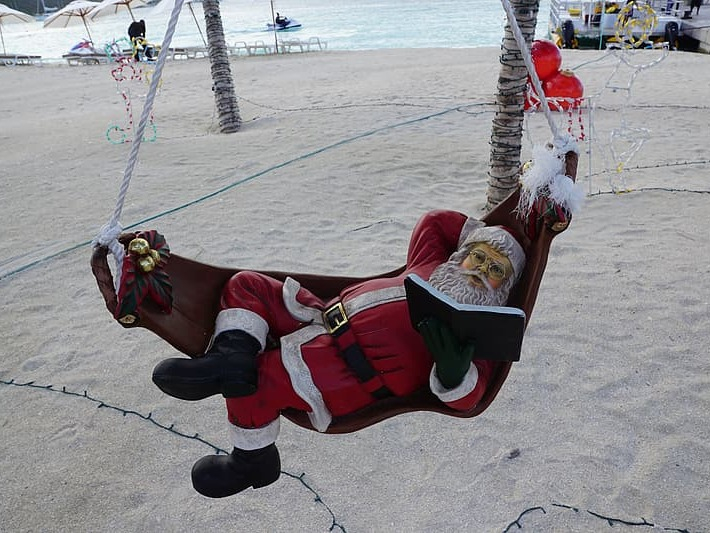 Santa on hammock reading a book near a body of water